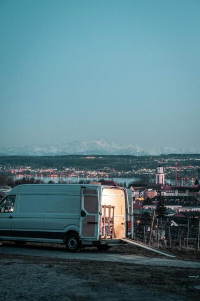 Otwarta furgonetka firmy Patryk Stok z Wrocławia zaparkowana na parkingu z widokiem na odległe ośnieżone góry pod czystym niebem podczas realizacji transportu krajowego mienia na długiej trasie.